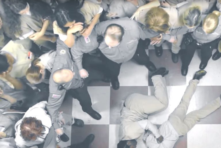 Taystee cries over Poussey's body while  correctional officers form a barrier between them and the other inmates. Image: Netflix.