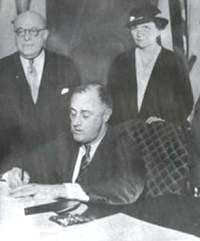 Perkins stands behind Roosevelt as he signs the National Labor Relations Act 